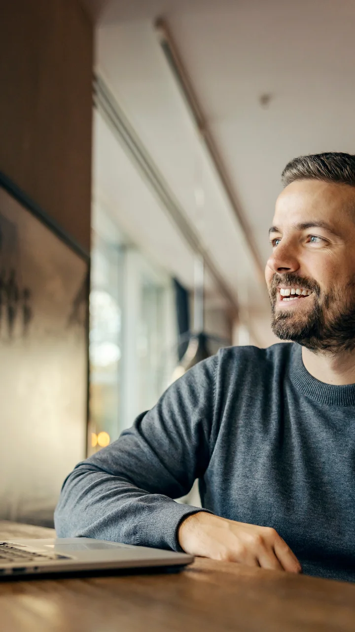 Bearded man at a café table with a laptop and a glass of orange juice