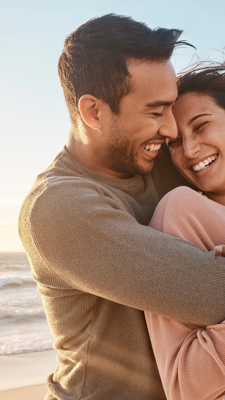 Couple laughing in an embrace on a beach at sunset