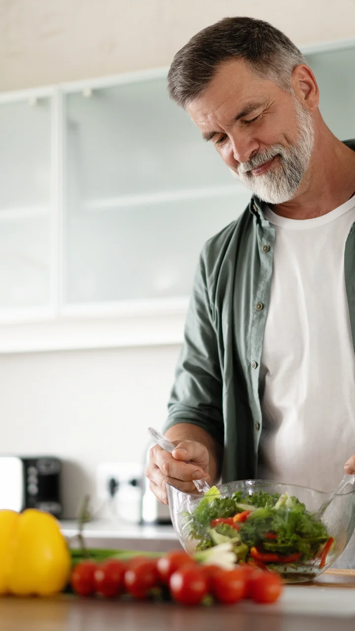 Mature man with a silver beard preparing a fresh salad in his kitchen