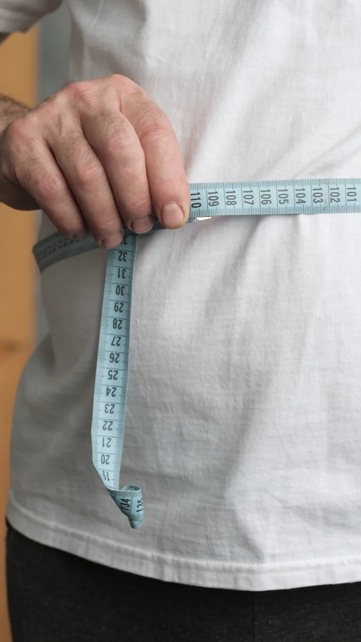 Cropped torso of a man in a white t-shirt measuring his waist with a tape measure